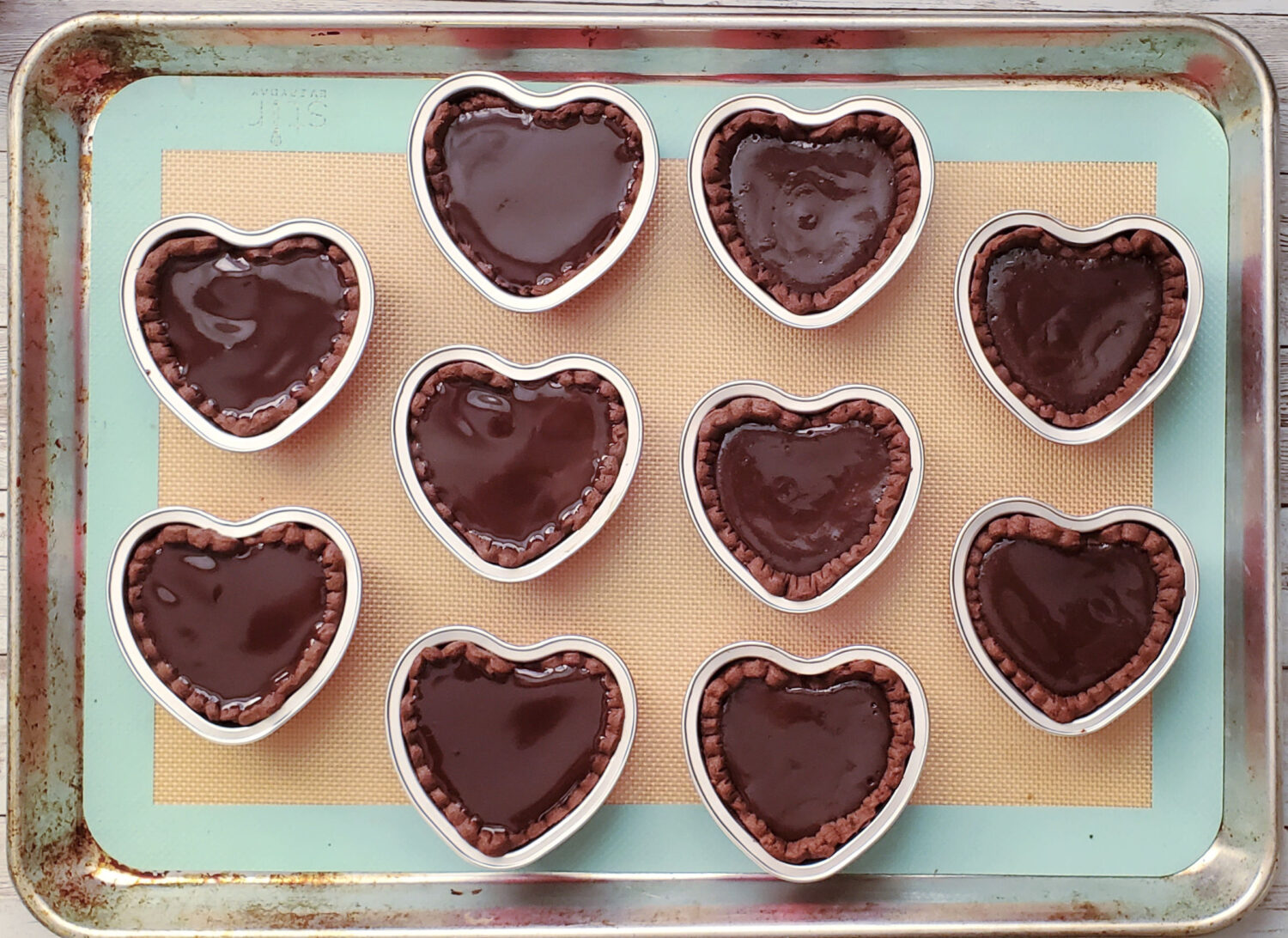 Decadent chocolate truffle filling in a dark chocolate crust, & a ganache glaze, baked into mini hearts. Perfect for Valentines Day!
